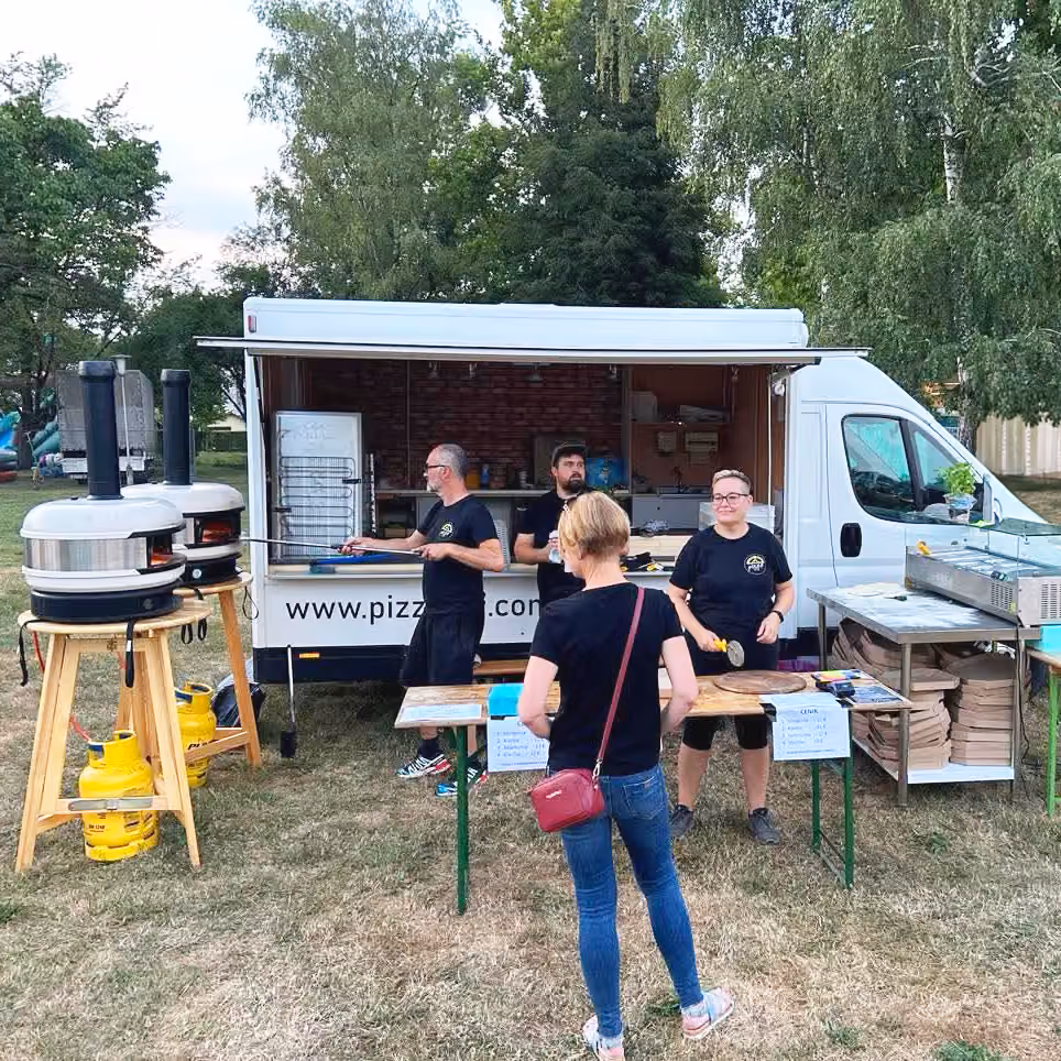 Pizzawagen mit Öfen bei einem Fest, Gäste davor