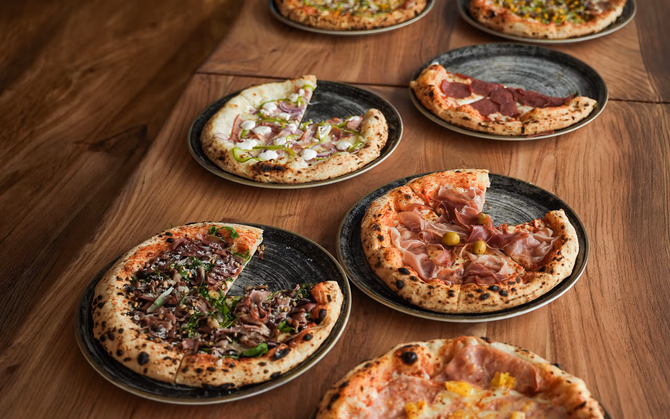 Frisch gebackene Pizzen auf einem Holztisch bei Pizza na i